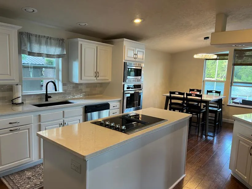 The same kitchen after remodeling, with white cabinets, quartz counters and hardwood floors